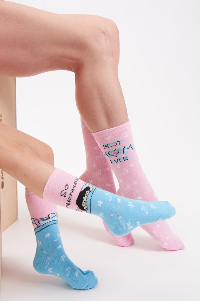 Pink women’s socks with moon and star graphics. Text on the adult socks says “Best Mom Ever” and text on kid socks says “So Embarrassing” with a picture of a small girl pulling bed covers up to her eyes.