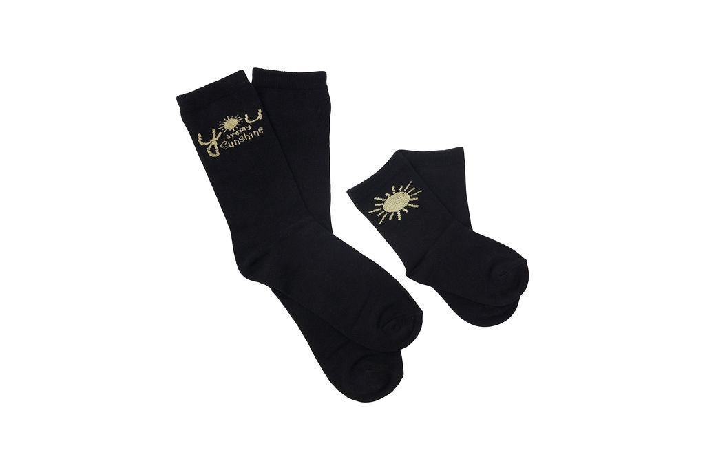 Black, women’s socks. Graphic says “You Are My Sunshine” on the adult socks with a picture of a sun on the kid socks.